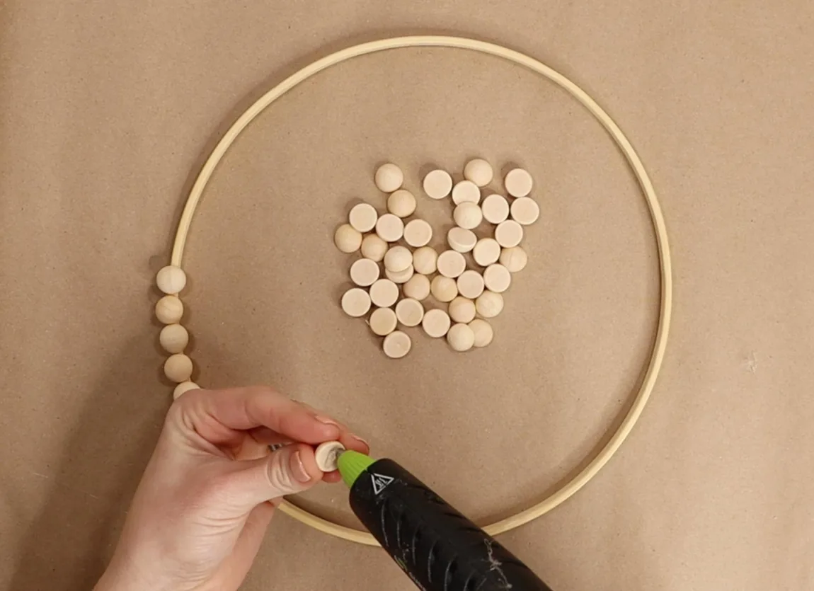 Using a wreath form of wood craft hoop to provide a sturdy base, I grabbed some 15mm wood bead slices close by and set to work using the hot glue gun. 